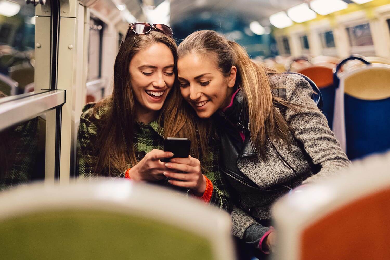 two girls on a train looking at a phone